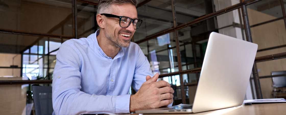 Professional gray haired white man with glasses looking at laptop in coworking space